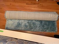 Rolled partially to show the beige woven backing and the thick blue shag pile texture of the rug, placed on a hardwood floor