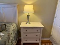 Full view of night table next to bed with lamp on top