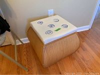 Side view of bamboo style storage hassock with white padded top decorated with blue spiral designs