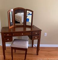 Full view of wooden vanity with tri-fold mirror and padded stool beneath