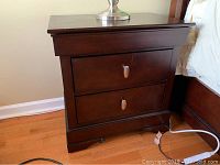 Front view of a dark brown night table showing two drawers and metal oval pulls
