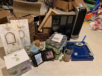 Photo showing tower fan, slicer box, mason jars, collage frame, scale, candles, wicker baskets, wood tray, first aid kit, and other miscellaneous household items.