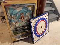 Full view of the vintage Pachinko game with metal balls visible, and Widdy dartboard leaning against it with three darts stuck on the board.
