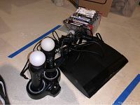 Sony PS3 Slim console with controller, charging dock with three motion controllers, and 13 games visibly stacked.