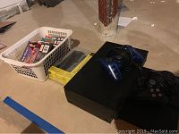 Image showing PlayStation 2 Phat console with two wired PS2 controllers (blue translucent and black) and basket containing game cartridges and DS Lite box.