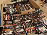 Overview of multiple PS2 game cases stacked on floor and in a cardboard box