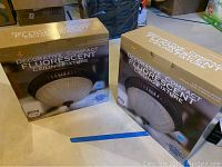 Two unopened boxed decorative compact fluorescent ceiling fixtures by Lights of America, size 15x15x7 inches, showing front and side views of the packaging.