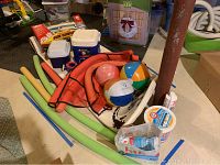 Overall view of pool accessories including pool noodles, coolers, noodle net, beach balls, foam pool float, and boxed RC boat.