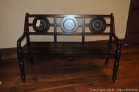 Full front view of dark wood bench showing slatted seat and backrest with three circular medallions