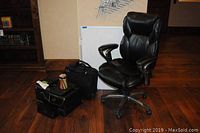 Full view showing black leather rolling office chair, computer bag, jar of colored pencils, white erasable board on floor.