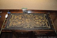 Full view of the leather scroll tapestry laid flat on a cabinet showing detailed etched floral patterns and metal rod support with four hanging loops.