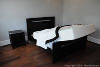 Full bed frame including headboard and footboard, foam mattress support, white comforter with black trim, and nightstand
