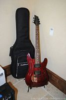 Laguna red electric guitar with soft black carrying bag behind it and guitar stand on floor.