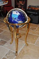 Full view of the gemstone world globe on gold-tone metal tripod stand showing the northern hemisphere side of the globe with blue ocean and light-colored continents.