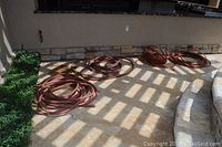 Four reddish-brown garden hoses coiled on patio floor, showing signs of use and wear.