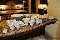 Full overview of set with plates, bowls, cups, mugs and serveware arranged on countertop.