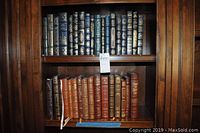 Two-shelf view of the leather-bound book collection in a wooden bookcase, showing dark blue books on top shelf and brown books below.