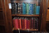 Wooden bookcase shelf with two shelves of leather-bound books; top shelf with black, teal and blue volumes; bottom shelf with red and burgundy volumes