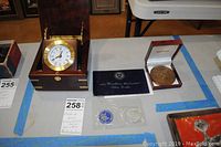 View of the three main items: wood case clock, Eisenhower silver dollar in blue certificate holder, and bronze medal in presentation case.