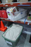 Plastic bins with scrap felt, beige drop cloths, and packing materials on shelving unit