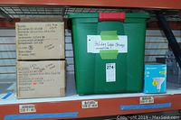 Two unopened boxes of Flextec LED rope lights with labels showing specifications and 'Never used' writing, next to a green bin labeled 'Holiday Light Strings Miniature' and a box of EcoSmart LED bulbs.