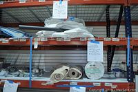 Overview of shelving displaying multiple cloth tarps folded and stacked, two partial rolls, and one full roll of Coolaroo heavy knitted shade cloth.