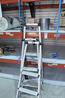 Two white aluminum stepladders shown on shelves, one about 3 feet and another 4 feet tall with anti-slip steps and handrails.