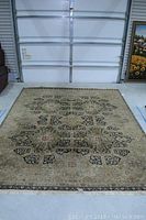 Full view of the large rectangular oriental style area rug placed on concrete floor in front of a garage door, showing wear and frays.
