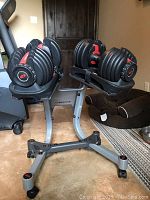 Adjustable dumbbells seated on stand next to weight bench in room