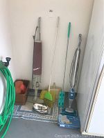 Full view of cleaning tools including electric broom, Swiffer, broom with dustpan, mop, garden hose and orange accessory on floor