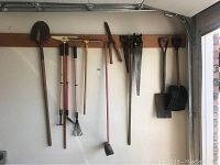 Photo showing the full set of garden tools arranged on a wall rack including shovel, rakes, broom, shears, saws, spade, and scoops.