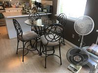 Dining set with round glass top table and four metal chairs with beige upholstered seats in kitchen area. Light wood flooring.