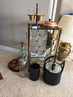 Full view of brass wine rack with multiple wine holders, black ice bucket and black container on floor, copper nut dish on top of the rack, wooden animal silhouette coasters on floor.