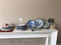 Photo showing various collector plates and tile coasters organized on a mantle by size and type.