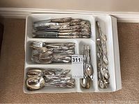 Full view of silverware set organized in white plastic tray, showing an assortment of forks, knives, spoons and serving pieces all with ornate handles.