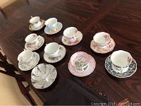 Ten assorted bone china teacup and saucer sets arranged on wooden table