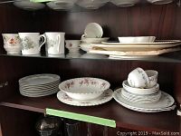Shelf with assorted English bone china including tea cups, saucers, plates, and bowls arranged in stacks.