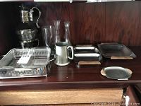 Multiple silver plated serving items including trays, a pitcher, and a mug displayed on a wooden surface.