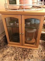 Light wood two-door cabinet with glass panes, placed on countertop with visible items inside