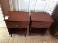 Pair of medium brown plywood night stands with single drawer and open shelf, viewed from front.