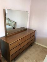 Front angled view of the mid century dresser with mirror showing nine drawers and wood finish.