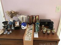 Overview photo of assortment of Asian and Greek decor on a wooden surface including multiple ceramic vases, figurines, a miniature screen, and jewelry box.