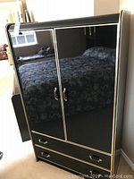 Front view of black lacquered wardrobe with gold trim and handles, two doors and two drawers.