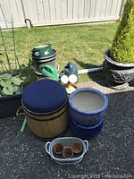 Photo showing items including wooden stool, two green watering cans, multiple ceramic and plastic garden pots in various sizes, and a white basket with small terracotta pots.