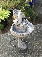 Full view of the garden fountain standing on concrete, showing wood-like textured pedestal and basin with bird sculptures on top.