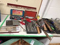 Wide photo showing assortment of socket wrenches, drill bits, hammers, and screwdrivers on a table.