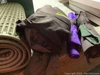 Camping gear including rolled green inflatable mat, folded tent, and folding chairs in covers