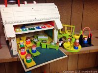 Overall view of Fisher Price Schoolhouse set with open front revealing classroom and wooden figures arranged inside, alphabet letters on display above desk area, playground accessories positioned to the side.