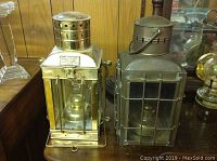Two brass hanging oil lanterns side by side on wooden surface, one polished brass and one older with patina