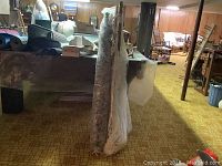 Two hammocks hanging side by side wrapped in protective plastic in large indoor space.